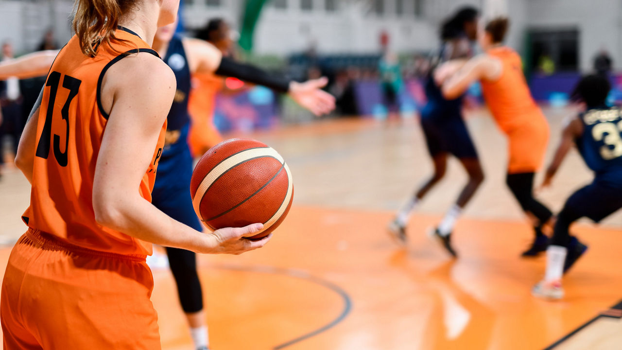 Basketball player in orange jersey holding a ball during a competitive game on a court.