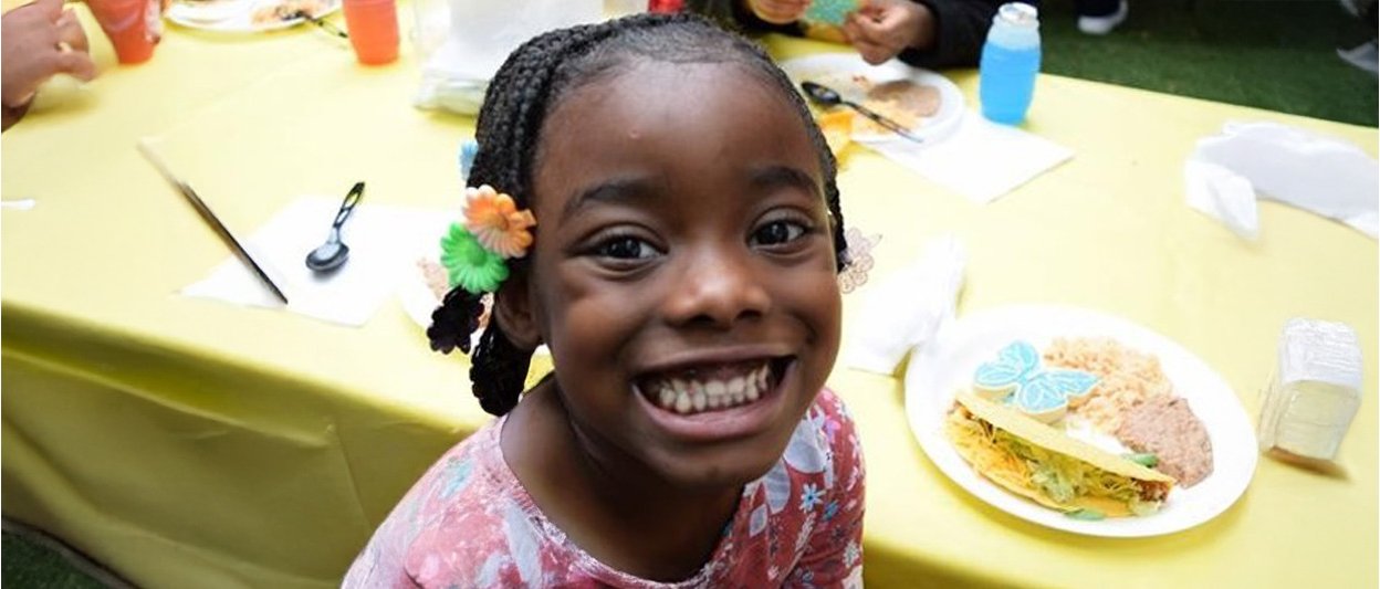 Plate of Mexican-inspired food featuring a taco, refried beans, and a butterfly-shaped cookie on a yellow tablecloth during a community meal event.
